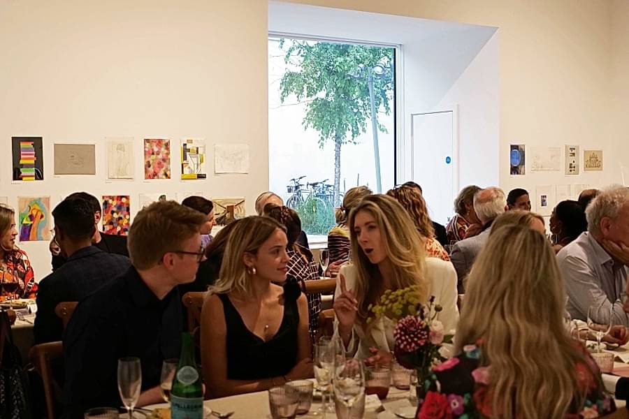 A group of people sat along trestle tables in a gallery space